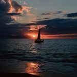 silhouette of sailboat on body of water during sunset